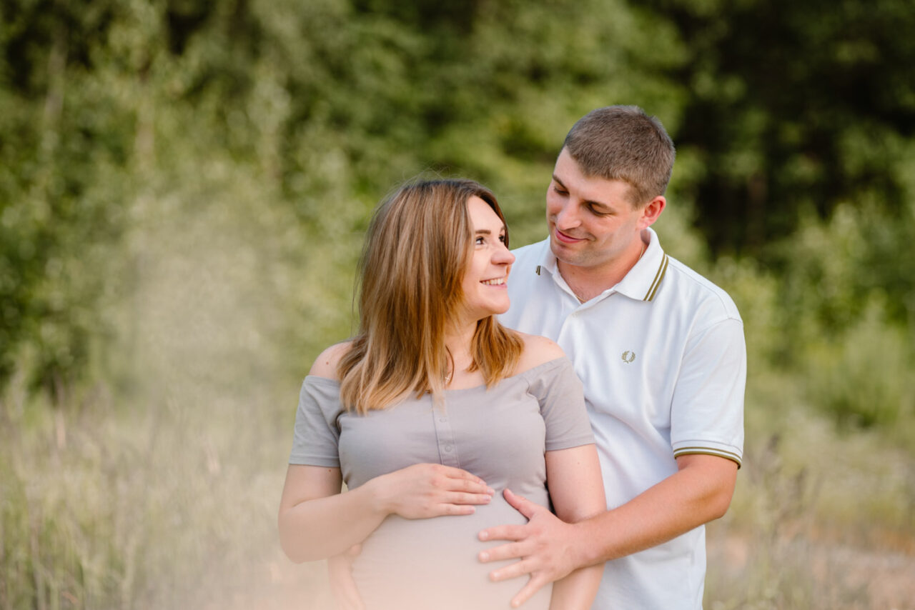 młody tato obejmuje swoją małżonkę w ciąży