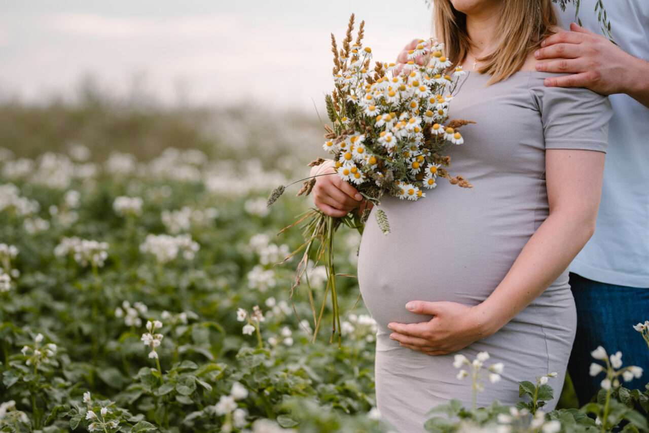 przyszła mama trzymająca brzuszek i bukiet polnych kwiatów
