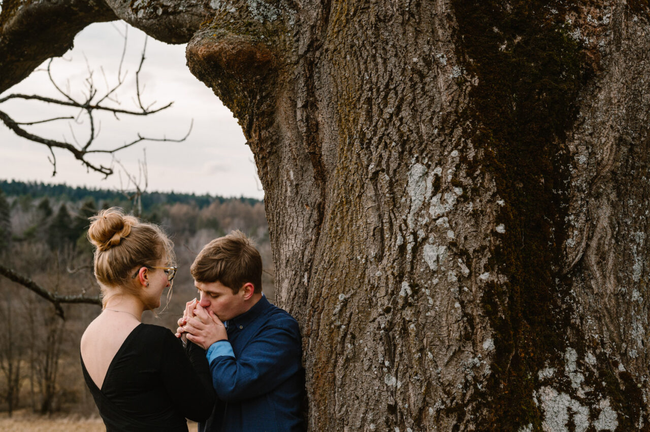 narzeczony całuje dłonie kobiety pod drzewem