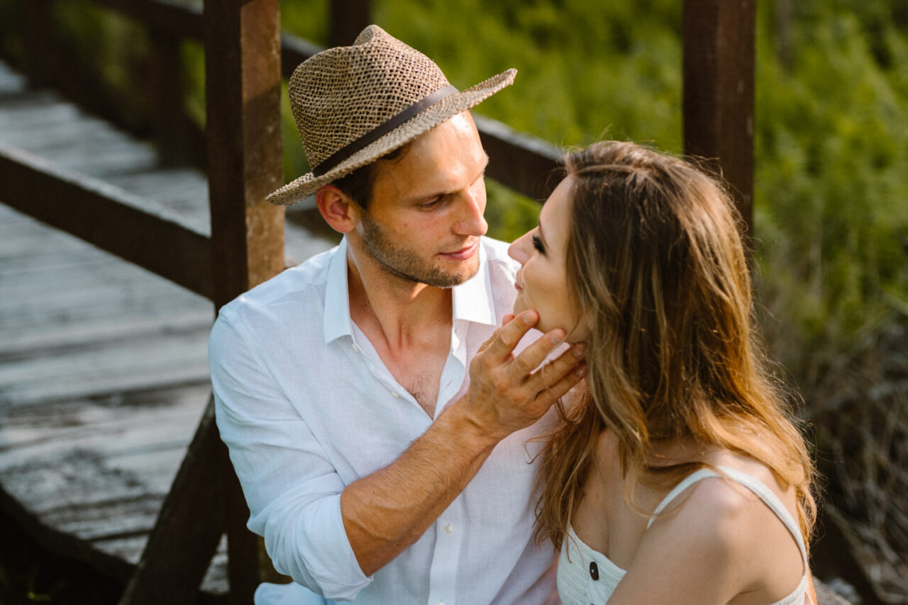 narzeczeni wpatrująsię w siebie na tle drewnianego mostu i łąk
